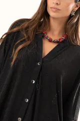 Camisa negra de corte oversize con diseño de encaje calado, escote en V, cierre frontal con botones y mangas tres cuartos. Presenta un diseño asimétrico con la parte posterior ligeramente más larga.