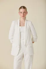 Saco de encaje blanco con solapas de satén, cierre frontal con botones y bolsillos laterales con solapa.