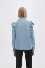 Camisa celeste de jean con cuello clásico, cierre frontal con botones y volados en el canesú delantero y trasero.