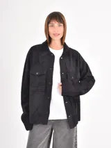 Campera de textura afelpada en color negro, con cierre frontal de botones a presión, cuello camisero y bolsillos frontales con solapa.