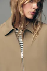 Chaqueta bomber negra con cuello solapa, manga larga abullonada y puños elásticos. Presenta falsos bolsillos de doble vivo en la parte delantera y cierre frontal con cremallera.