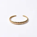 Brazalete rígido dorado con diseño trenzado.