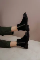 Bota corta de cuero gamuzado color marrón chocolate, con punta cuadrada y suela track. Presenta una correa con hebilla desmontable y cierre lateral con cremallera.