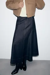 Falda midi de denim en color azul oscuro, con diseño evasé, bolsillos delanteros, costuras pespuntadas en contraste y cierre frontal con cremallera y botón metálico.