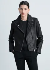 Campera estilo biker de cuero ovino negro, con solapas amplias, cierre frontal asimétrico, bolsillos laterales con cremallera y detalles de tachas metálicas en el cuello.