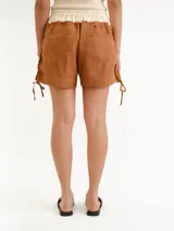 Short marrón claro de lino, con cintura elástica de color blanco crudo y detalles de lazos laterales en las botamangas.