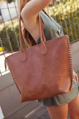 Bolso tote de cuero color tostado con costuras blancas a la vista en los laterales y doble asa de hombro.