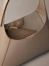 Cartera tipo hobo mediana Calvin Klein de poliuretano color beige, con diseño estructurado, costuras pespunteadas y correa ajustable con hebilla metálica dorada.
