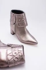 Botas cortas de cuero negro con taco cuadrado y punta fina. Presentan cuello caído capitoneado con apliques brillantes y cierre lateral con cremallera.