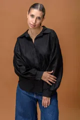 Camisa negra de corte clásico con mangas largas abullonadas y puños abotonados. Presenta paneles de encaje floral en la parte superior delantera y trasera, combinando texturas con un diseño elegante y sofisticado.