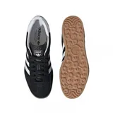Championes Adidas Gazelle Indoor de diseño clásico, confeccionados en gamuza negra con las icónicas tres tiras laterales en blanco. Presentan el nombre del modelo en letras doradas, talón en contraste blanco y suela de goma color caramelo.