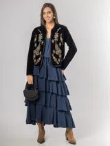 Falda midi de micro corderoy azul marino, con diseño de volados escalonados y cintura elástica. Presenta un corte asimétrico, siendo ligeramente más corta en la parte frontal.