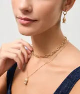 Conjunto de bijouterie compuesto por dos collares en capas y un par de aros tipo argolla con dije de flor. Uno de los collares presenta eslabones ovalados, mientras que el otro es una cadena fina con pequeñas esferas y un dije central de flor en relieve. Los aros incluyen el mismo diseño de dije floral colgante.