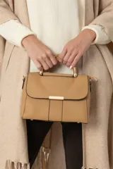 Cartera color beige de símil cuero con asa corta rígida combinada metal con cuero, broches metálicos dorados, cierre y asa larga para colgar.