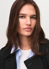 Abrigo tipo trench color negro, de diseño recto y cruzado con cierre de botones. Cuenta con cuello de solapa, mangas largas con trabillas en los puños, cinturón ajustable y dos bolsillos laterales.