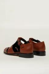 Sandalia cerrada tipo pescador, color blanco o hueso brillante, con tiras entrecruzadas en el empeine y cierre de hebilla ajustable en el lateral. Posee suela y taco bajo de color negro.