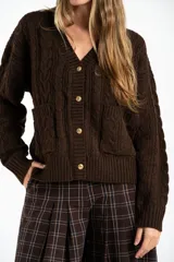 Cardigan de punto con diseño de trenzas, color marrón oscuro, con escote en V, cierre frontal de botones dorados y bolsillos delanteros.