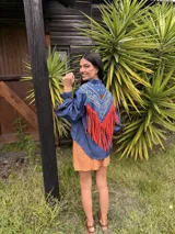 Camisa de jean con diseño estilo western, featuring un canesú trasero con estampado paisley en blanco y azul, y flecos largos de cuero rojo. Cuenta con mangas largas abullonadas con puños elásticos fruncidos.