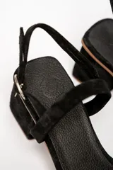 Sandalias de cuero color negro, con taco cuadrado bajo y tira delgada sobre los dedos.