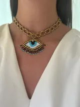 Gargantilla de cuentas doradas con dije de ojo turco hecho con cuentas blancas, celestes, negras y marrones.