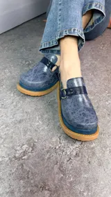 Zuecos cerrados tipo sandalias de plataforma, confeccionados en cuero con efecto craquelado en tono azul, con tiras texturizadas, argollas metálicas decorativas y tira trasera con hebilla regulable.
