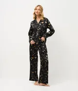 Pijama de dos piezas confeccionado en satén con estampado floral sobre fondo negro. La blusa es estilo camisa con cuello solapa, manga larga y cierre frontal con botones. El pantalón cuenta con cintura elástica y corte recto.