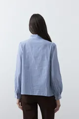 Camisa de rayas verticales con cuello mao, detalle de volados en el escote, bordados florales y recortes con calados. Posee mangas largas abullonadas con puños ajustados y cierre frontal con botones.