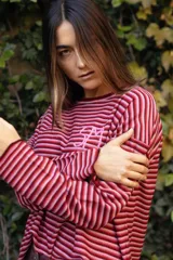 Remerón de manga larga y tejido de punto, con diseño de rayas finas horizontales en tonos rojos y rosados. Presenta cuello redondo y logo bordado a mano en el pecho.