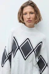 Media polera de tejido de punto color crudo, con diseño de rombos en el frente en tonos gris y negro. Presenta cuello alto y mangas largas.