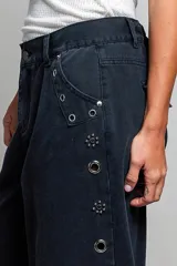 Pantalon de tiro bajo y pierna ancha confeccionado en denim negro con efecto vintage, decorado con ojales metálicos a lo largo de los laterales y los bolsillos.