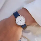 Reloj de pulsera Skagen modelo Signatur con caja de acero en tono oro rosado, esfera blanca minimalista y correa de cuero azul.