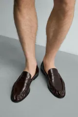 Mocasín de vestir negro de estilo clásico con detalle de antifaz en la parte superior, suela a tono y ligero tacón.