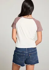 Remera blanca con mangas cortas color marrón y estampado frontal con la palabra "CIAO" en celeste con estrellas rosadas.