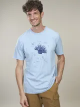 Remera de algodón color celeste, con cuello redondo y manga corta. Presenta un estampado frontal de un diseño botánico en tonos azules y texto.