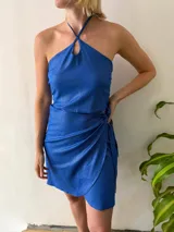 Conjunto de dos piezas color azul brillante, compuesto por un top halter con breteles finos y lazo regulable en el contorno, y una falda corta cruzada regulable.