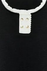 Top negro de manga corta y cuello redondo, confeccionado en hilatura con mezcla de algodón. Presenta ribetes en contraste de color blanco con detalles de volados en el cuello y las mangas, y cierre frontal parcial con botones dorados.