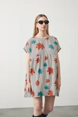 Vestido corto de silueta amplia con corte bajo busto, cuello a la base y mangas cortas. Presenta un estampado de lunares negros sobre fondo beige claro.