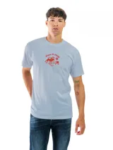 Remera de algodón color celeste claro, con cuello redondo y manga corta. Presenta un pequeño estampado frontal en color rojo con la frase "Pizza & Chill" y una ilustración de un perro sobre un sillón.