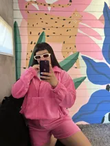 Conjunto deportivo de plush color rosa chicle, compuesto por un buzo oversize con capucha, bolsillo, cuello con cierre y elástico ajustable en la cintura, y un short.