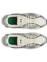 Championes UA Sola de diseño deportivo y retro, en colores blanco, plateado y verde. Cuenta con parte superior de malla ligera, superposiciones metálicas, entresuela de EVA acolchada y detalles en verde en la suela y los laterales.