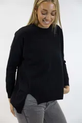 Buzo de punto negro, con cuello redondo, mangas largas y dobladillo asimétrico con aberturas laterales.