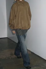 Chaqueta tipo bomber fluida color tostado, con cuello alto ajustable mediante cordones, cierre frontal con cremallera y botones a presión ocultos bajo solapa. Presenta mangas largas con puños elásticos, bolsillos delanteros y bajo con pliegues.