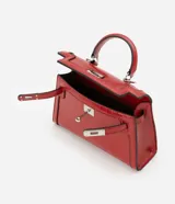 Cartera pequeña de poliuretano color rojo, con diseño estructurado, asa superior rígida y cierre frontal con herraje metálico.