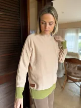 Sweater de punto en color beige con cuello alto y detalles en color verde oliva en los puños y el ruedo. Presenta un diseño holgado con parche de marca en el lateral.