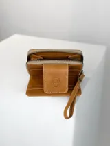 Mini billetera de cuero marrón con solapa frontal que presenta un grabado de un búho. El cuerpo de la billetera está confeccionado en cuero con pelo natural en tonos marrones y manchas doradas.