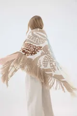 Ruana de punto triangular tejida en lambswool, con diseño geométrico en tonos tostado, blanco y negro, terminada con flecos en los bordes.