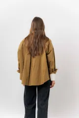 Sobrecamisa de gabardina liviana color crema, con corte oversize, cuello clásico, cierre frontal con botones a presión y dos bolsillos delanteros con solapa.