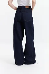 Pantalón de jean azul oscuro, de corte wide leg y tiro alto, con costuras a la vista y cierre frontal con botón.