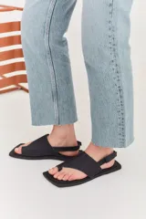 Sandalias de cuero negro con diseño de punta cuadrada, tira ancha sobre el empeine y ajuste con correa en el talón.