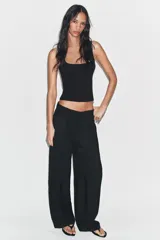 Pantalón negro de tiro alto y pernera ancha, confeccionado en tejido fluido, con bolsillos laterales y detalles de pliegues en la parte delantera.